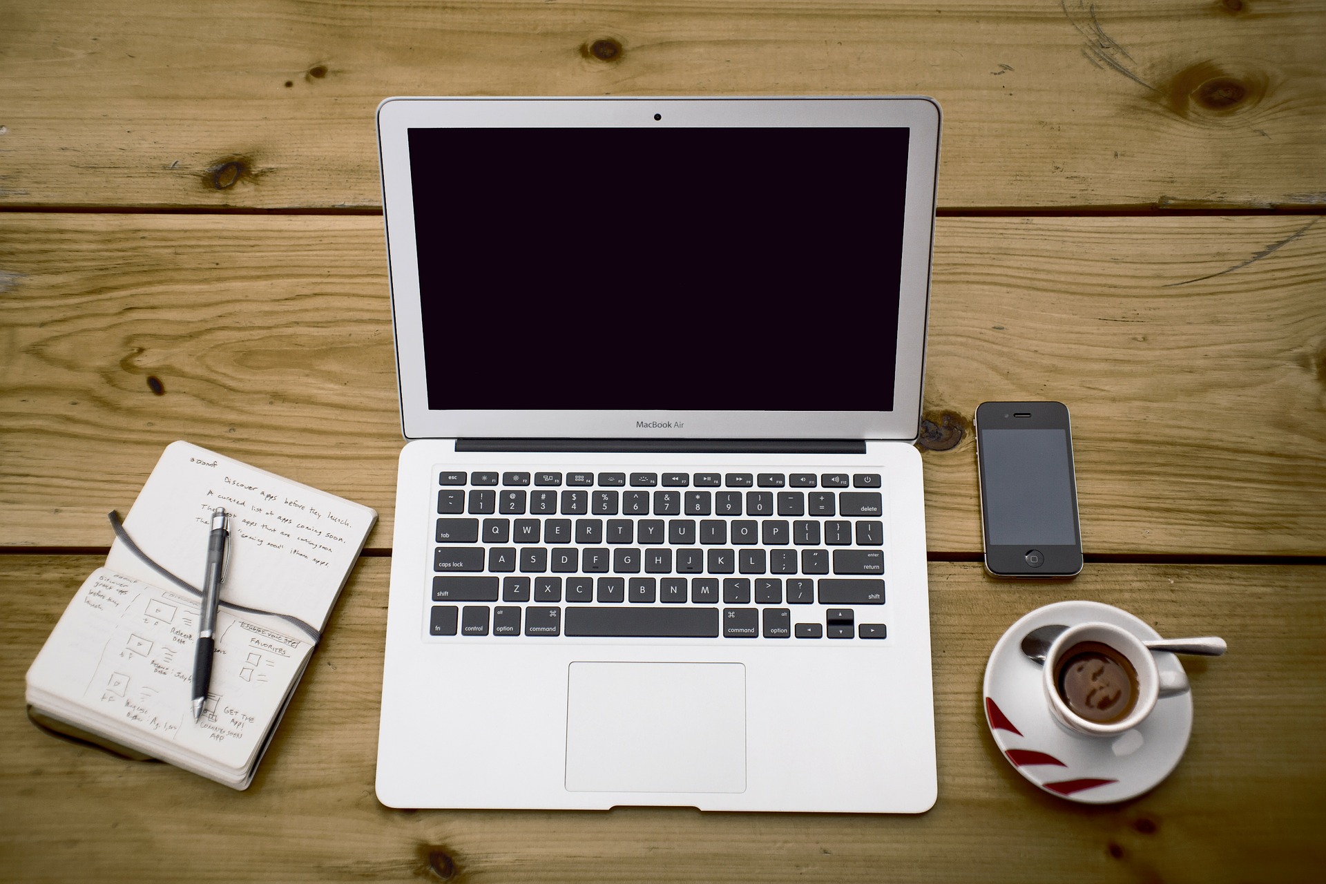 Slika prikazuje radni stol s laptop uređajem, mobilnim aparatom i notesom sa bilješkama.